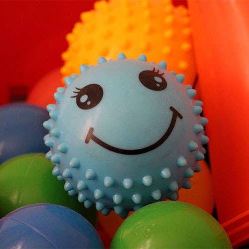 Bunte Bälle, die auch in der Ergotherapie verwendet werden können. Auf einem blauen Ball ist ein fröhliches Gesicht.