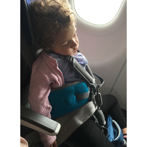 Das kleine Mädchen mit SMA Typ 1 sitzt schlafend auf einem speziellen Kindersitz im Flugzeug.