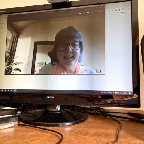 Eine Webcam zeichnet SMA-Patientin Camilla auf, sodass sie im Bildschirm eines Monitors auf einem Arbeits-Schreibtisch zu sehen ist.