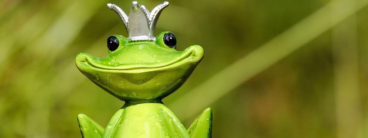 Eine Gartenfigur sitzt auf einer Mauer. Der grüne Frosch stellt eine Märchenfigur dar und trägt eine Krone.