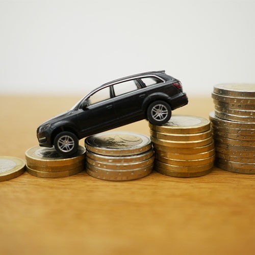 Ein schwarzes Spielzeug-Auto steht auf Stapeln aus Euro-Münzen. Das Vorderteil des Autos steht auf einem niedrigeren Stapel. Dadurch neigt sich das Auto nach unten.
