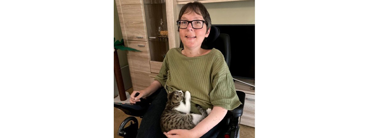 SMA-Patientin Camilla sitzt im Rollstuhl und hält ihre Katze im Arm.