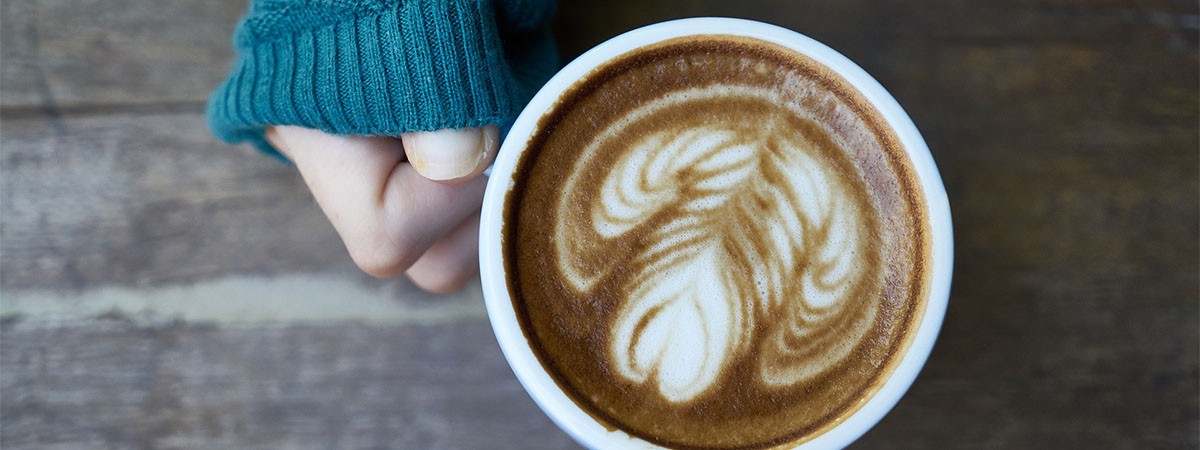 Eine Hand hält eine Kaffeetasse mit verziertem Milchschaum.