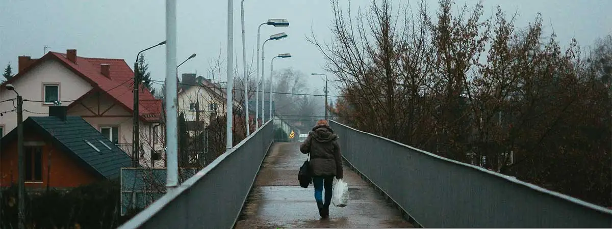 Ein düsteres, negativ geprägtes Bild einer regennassen Brücke, über die eine dunkel gekleidete Person läuft.