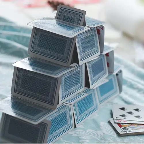 Ein Haus aus Spielkarten auf einer hellblauen Tischdecke. 