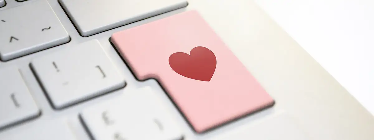 Foto vom Ausschnitt einer weißen Laptoptastatur mit einer rosa Entertaste, auf der ein rotes Herz abgebildet ist.