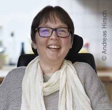 Portrait-Foto der 49-jährigen SMA-Patientin Camilla. Das Redaktionsmitglied sitzt im Rollstuhl und lächelt in die Kamera.